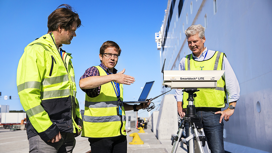 Tre anställda på teknikenheten i varselkläder på kajen