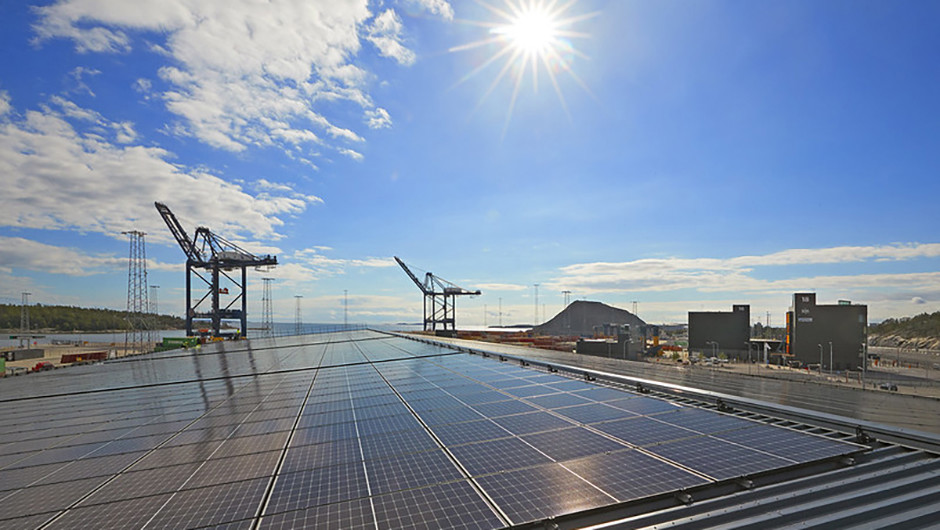 Solcellsanläggning i förgrunden och två containerkranar i bakgrunden.