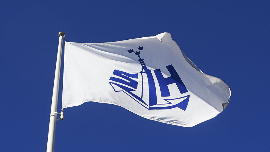 Flagga med Stockholms Hamnars logotyp som vajar i vinden med en blå himmel i bakgrunden