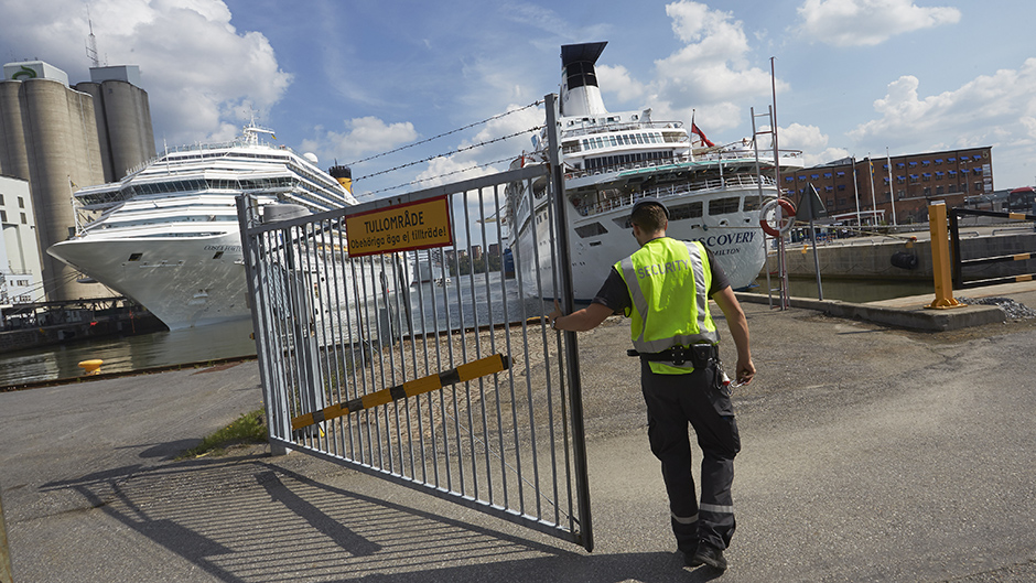 En väktare stänger en grind i Frihamnen. Två kryssningsfartyg i bakgrunden.