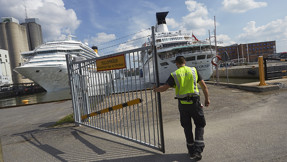 En väktare stänger en grind i Frihamnen. Två kryssningsfartyg i bakgrunden.