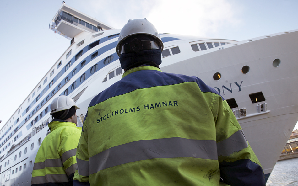 I förgrunden två personer i varselkläder, i bakgrunden en stor färja.