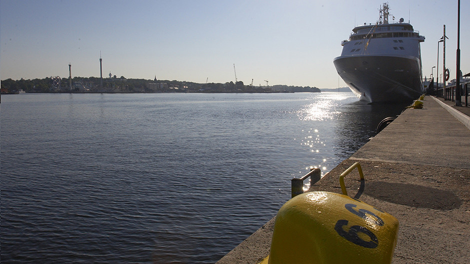 Vatten, kaj och en gul pollare i förgrunden, ett kryssningsfartyg i bakgrunden.