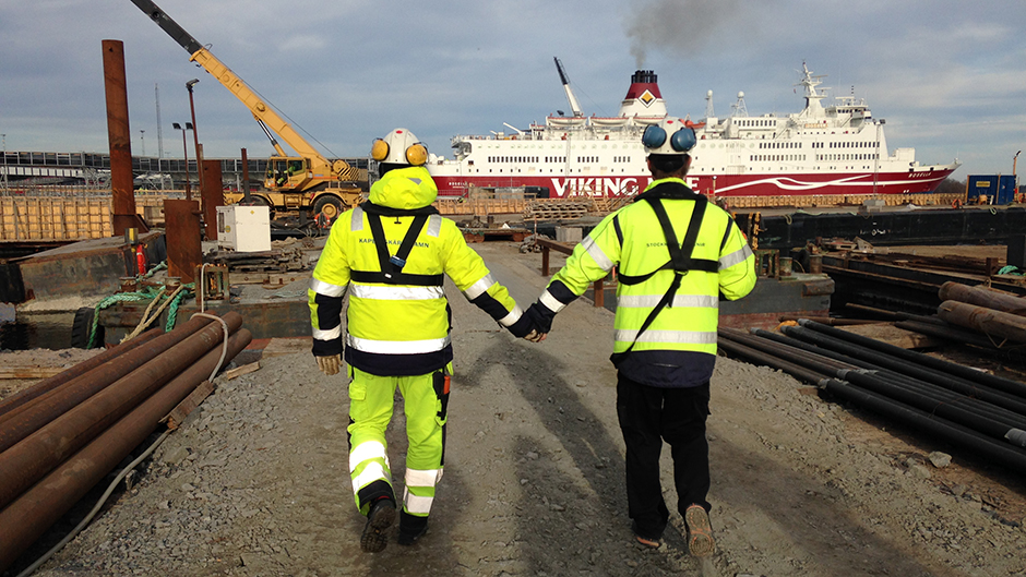 Deltagare i projektet och anställd i hamnen går hand i hand med fartyget Rosella i bakgrunden
