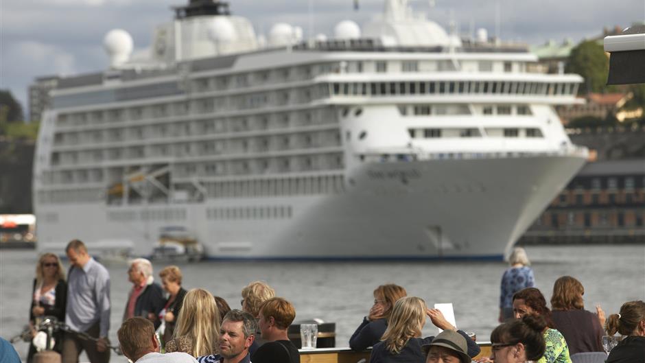 Kryssningsfartyg på Strömmen med människor i förgrunden på kajen.