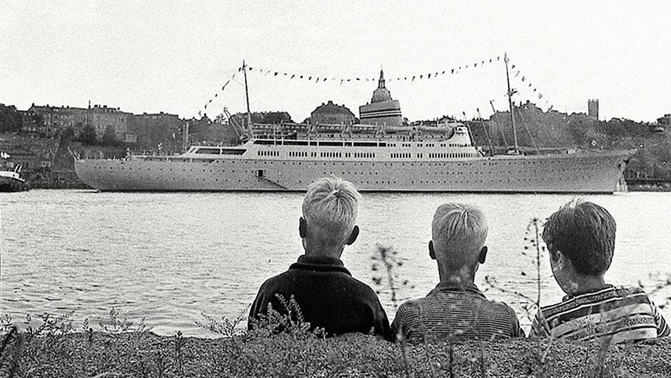 Tre pojkar beskådar kryssningsfartyget Oslofjord som ligger för ankar på Stockholms ström.