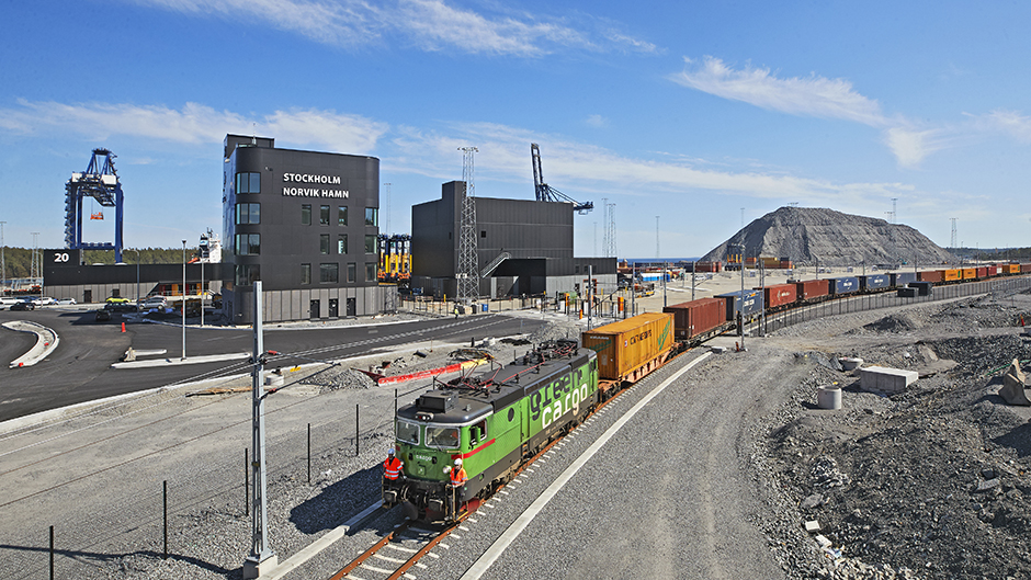 Fullastat godståg på spåret i Stockholm Norvik Hamn. I bakgrunden syns fler byggnader och två kranar.