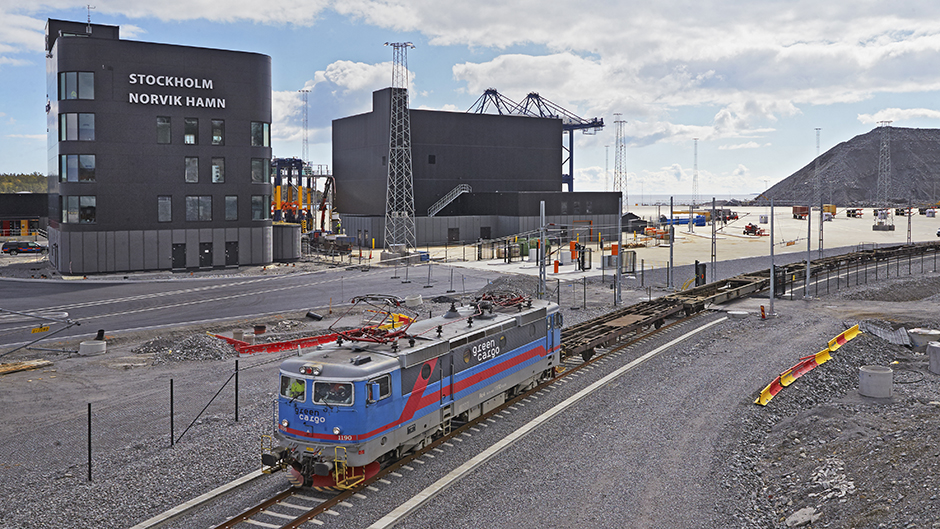 Tåg på spår med byggnader och kranar i bakgrunden