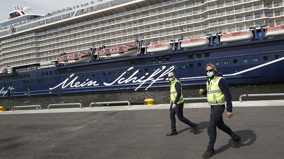 Två hamnstyrmän med munskydd framför Mein Schiff 1