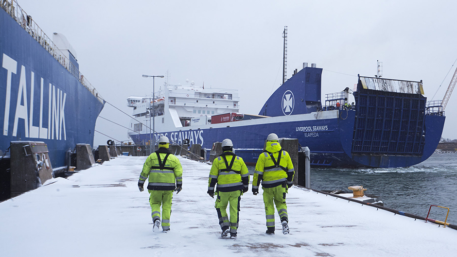 Tre stuveriarbetare på en snöig kaj med två roro-fartyg i bakgrunden