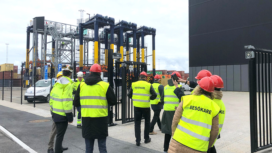 Besökare i varselvästar framför grensletruckar i Stockholm Norvik Hamn