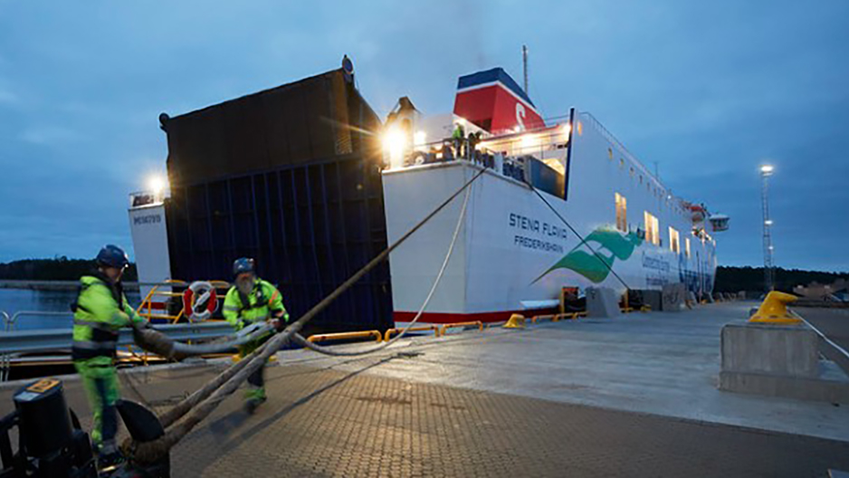 Två hamnarbetare håller på och förtöjer Stena Flavia i Stockholm Norvik Hamn på kvällen